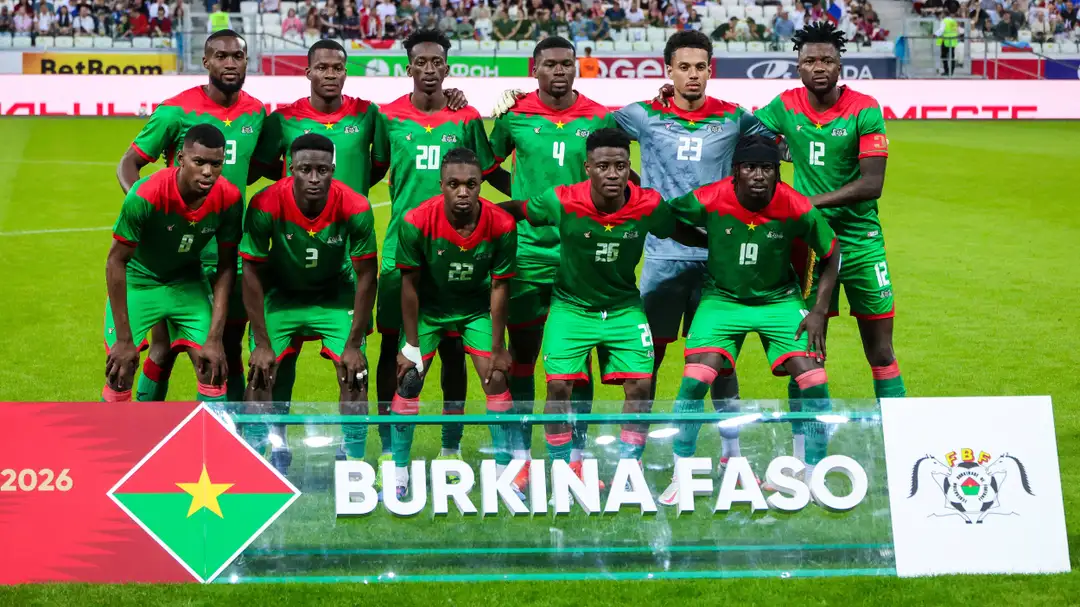 Sebelas pemain mengenakan seragam hijau dan merah berpose dalam dua baris di lapangan sepak bola dengan papan bertuliskan Burkina Faso di depan mereka